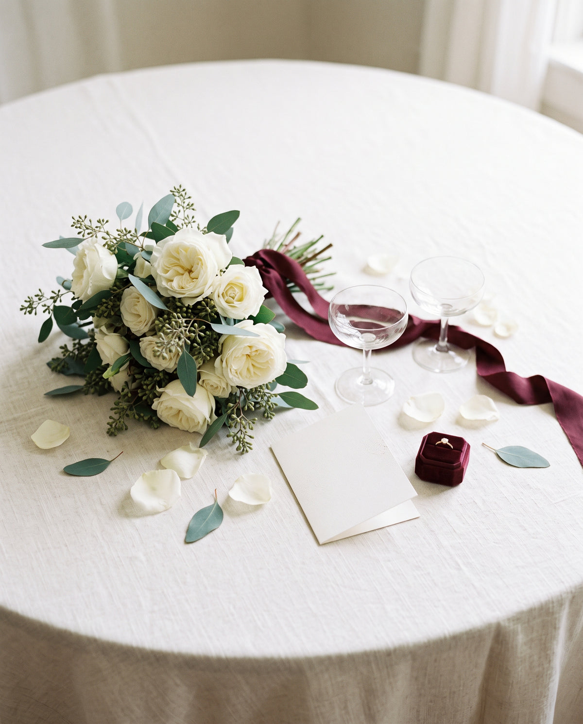 Bruidsboeket, champagneglazen, een kaartje en een ringdoosje op een linnen tafel